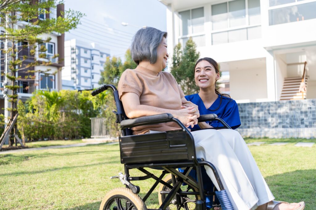 Asian happy senior woman patient sitting on wheelchair at green park.